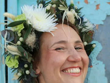 Woman with flower wreath smiles in front of blue wall.