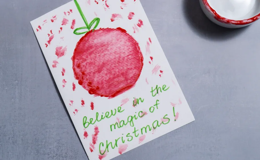 Weihnachtskarte mit gemaltem Ornament auf Tisch.