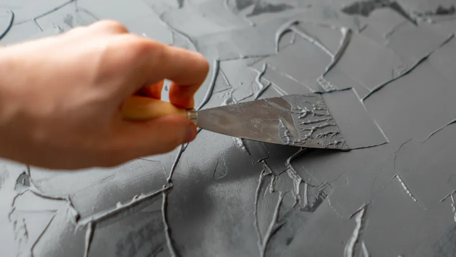 Hand smoothing gray plaster on wall.