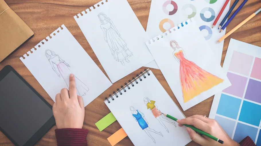 Modezeichnungen auf Papier, mit Bleistiften in der Nähe.