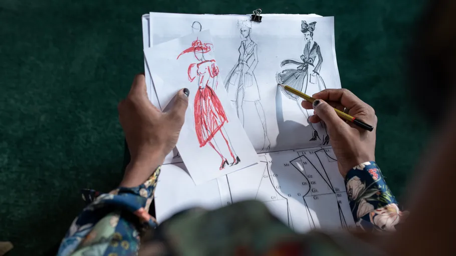 Person drawing fashion sketches on paper.