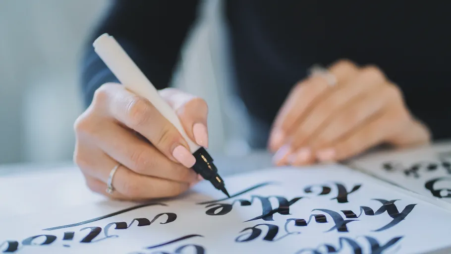 Hände schreiben Kalligraphie mit einem Stift.