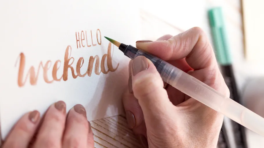 Hand schreibt 'Hello weekend' auf Papier.