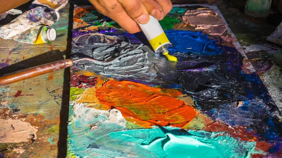 Hand squeezing paint onto colorful palette.