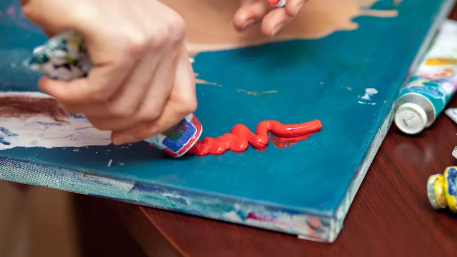 Person squeezing red paint onto canvas.