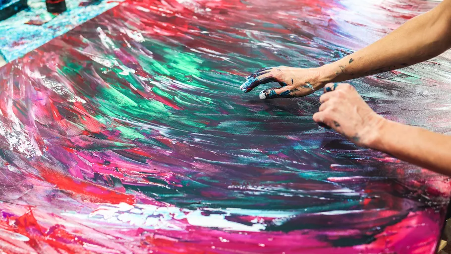 Hands finger-painting abstract art on canvas.