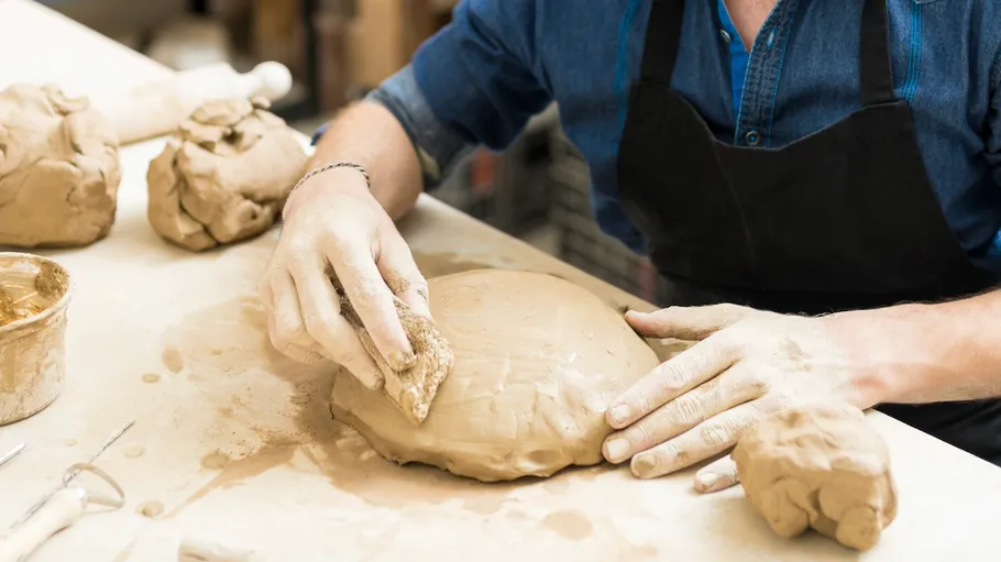 Person crafting clay sculpture on workbench.