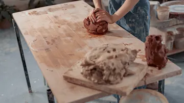 Person kneading clay on wooden table.