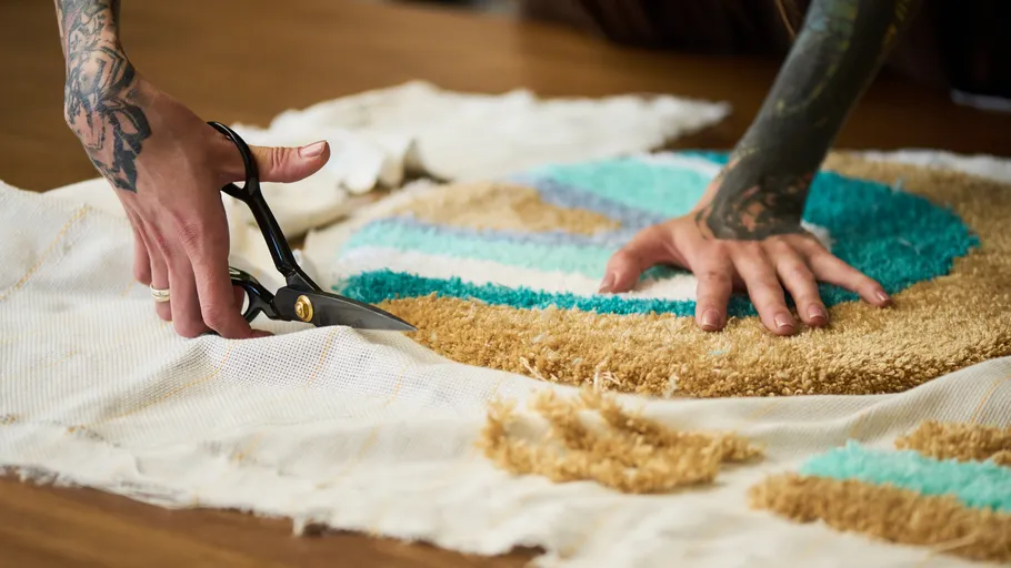 Hände schneiden bunten Teppich auf Tisch.