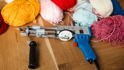 Tufting-Pistole und bunte Garne auf dem Boden.