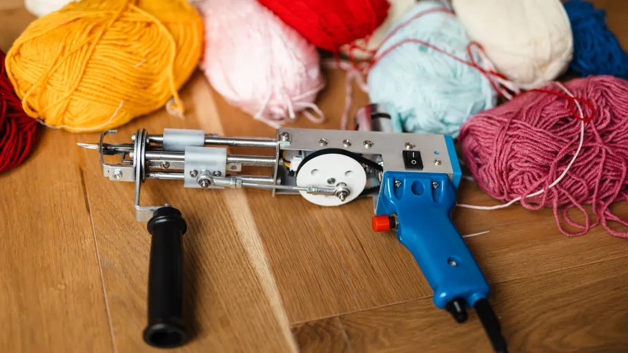 Tufting gun and colorful yarn on floor.