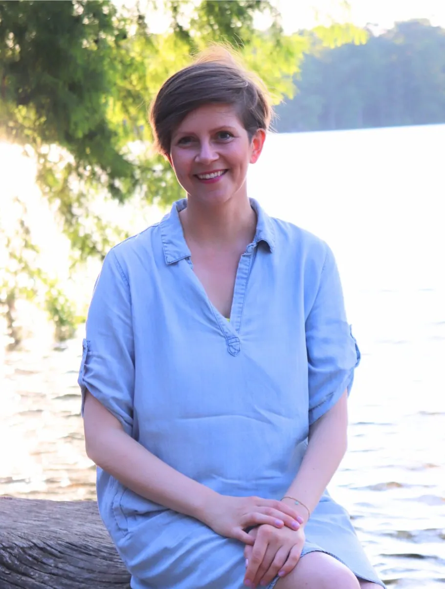 Person sitting smiling by a lake.