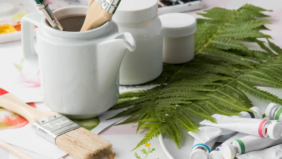 Art supplies with fern leaves on table.