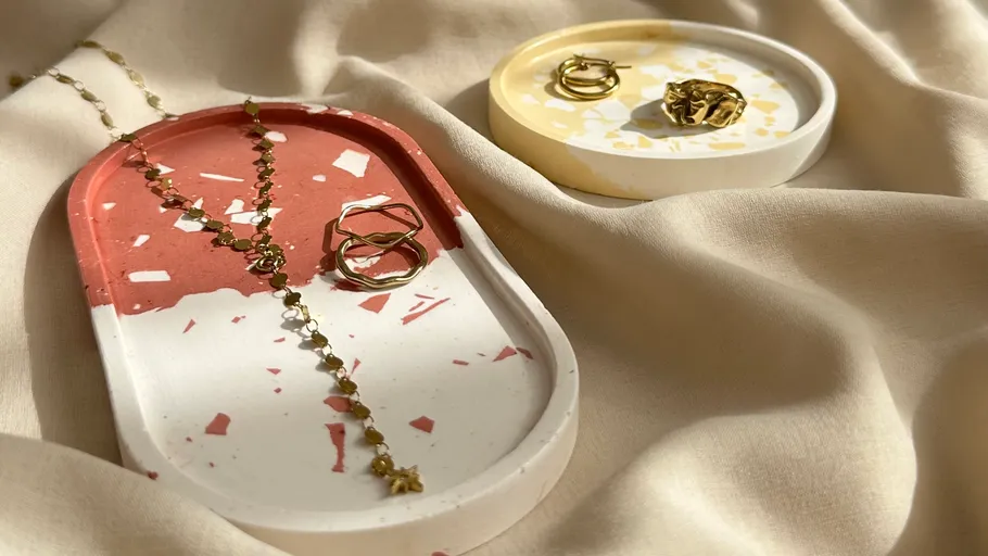 Schmuck auf Terrazzo-Tabletts mit Stoffhintergrund dargestellt.