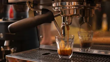 Espressomaschine gießt Kaffee in Glas.