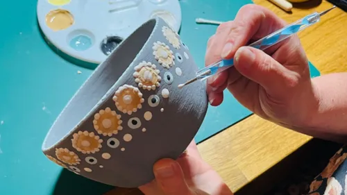 Person decorates bowl with floral designs.