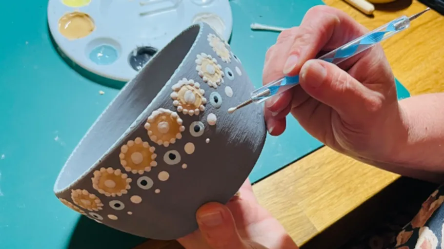 Person decorates bowl with floral designs.