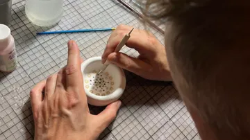 Person malt kleine Punkte auf Keramikobjekt.