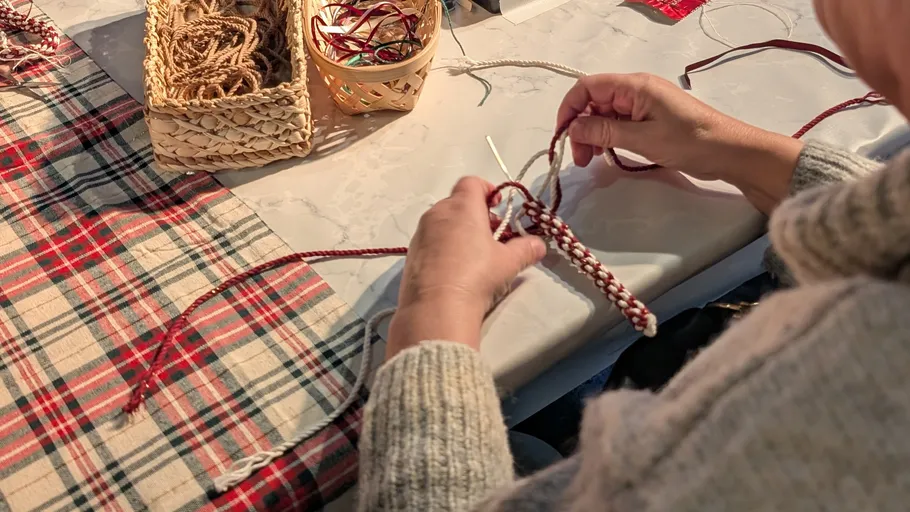 Person braiding a cord on a table.