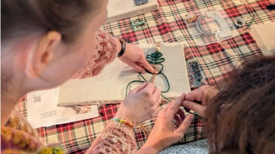 Two people embroidering on fabric, plaid table.