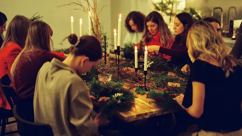 Women making wreaths around a candlelit table.