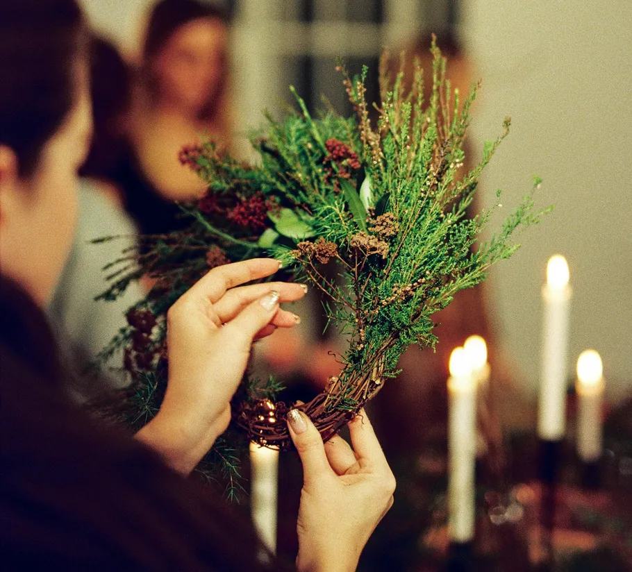 Person gestaltet Kranz an Kerzentisch.