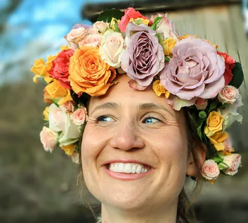 Frau mit Blumenkranz lächelt vor einem natürlichen Hintergrund.
