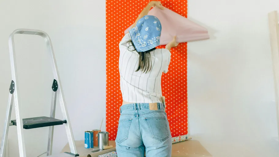 Woman applying wallpaper on wall near ladder.