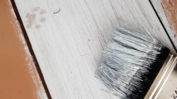 Pinsel auf halb gestrichener Holzoberfläche.