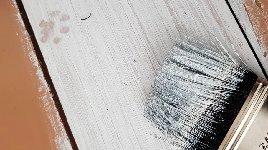 Pinsel auf halb gestrichener Holzoberfläche.