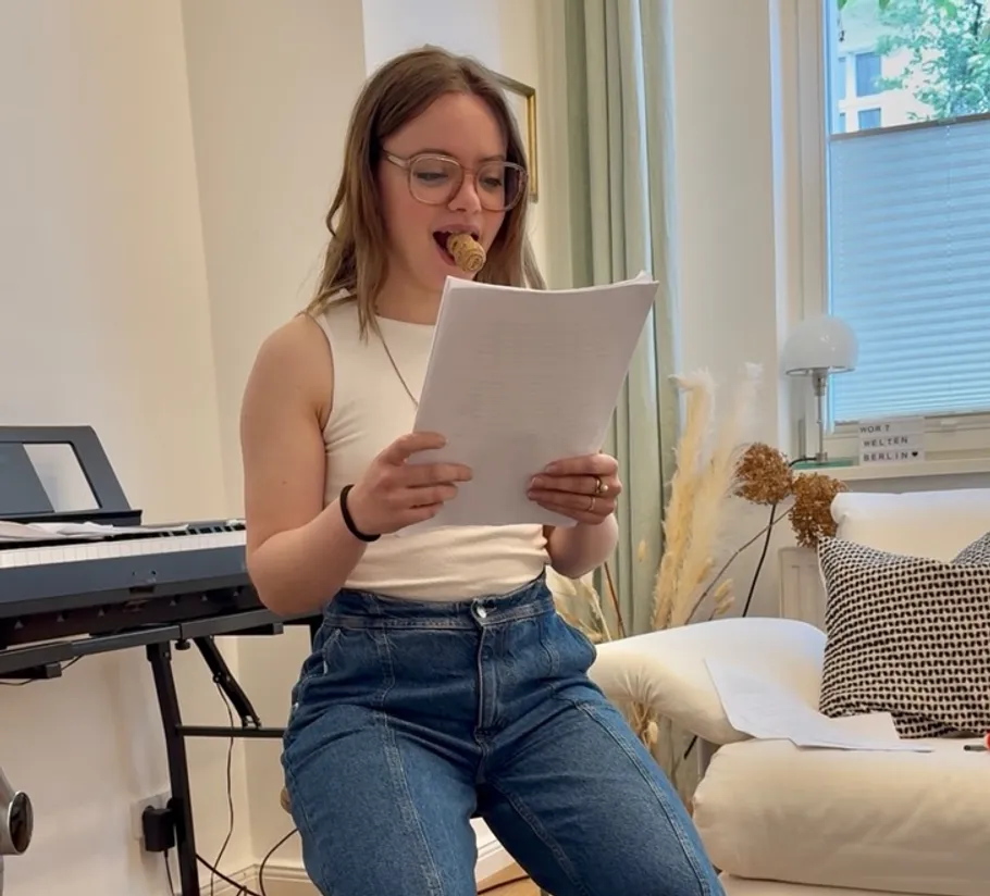 Woman reading paper with ice cream in mouth.
