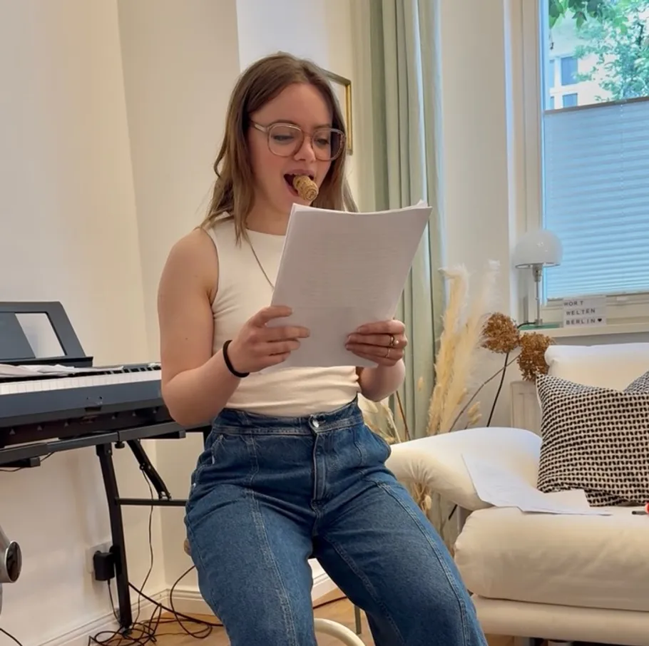 Person liest Papiere mit Stift im Mund drinnen.