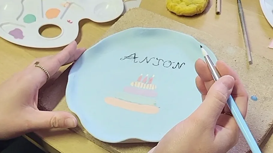 Hands painting plate with name and cake.