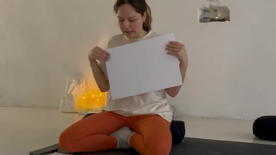 Person holding paper seated on yoga mat.