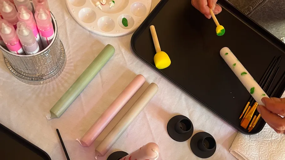 Person bemalt bunte Kerzen auf einem Tisch.