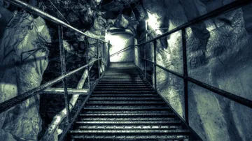 Metalltreppe führt in beleuchtete Höhle hinab.