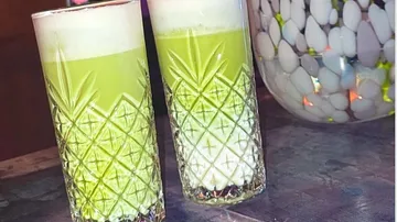 Zwei grüne Cocktails in Muster-Gläsern auf Tisch.