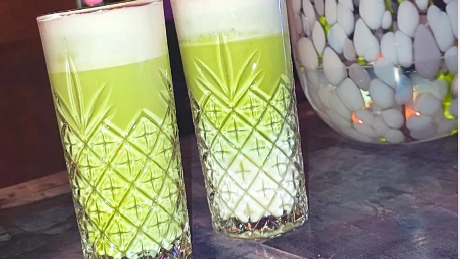 Zwei grüne Cocktails in Muster-Gläsern auf Tisch.