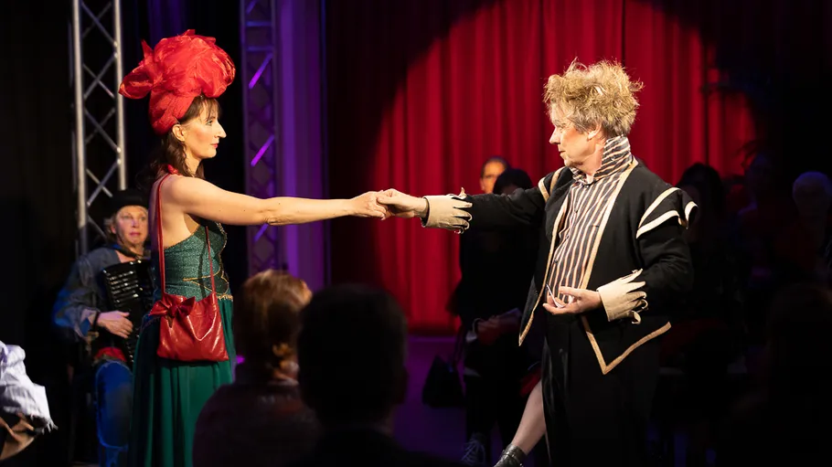 Two performers on stage in dramatic costumes.