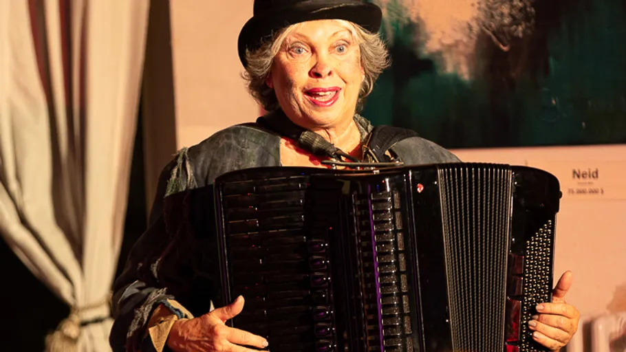 Woman playing accordion on stage with curtains.