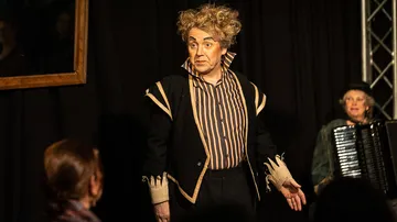 Performer in costume on stage with accordion player.
