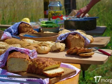 Bread is lying on an outdoor table, someone is cooking.