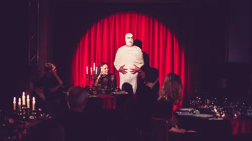 Performer on stage in white costume, audience watching.