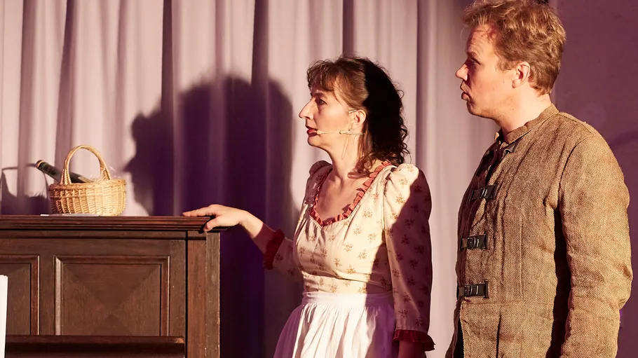 Two actors performing on stage with basket.