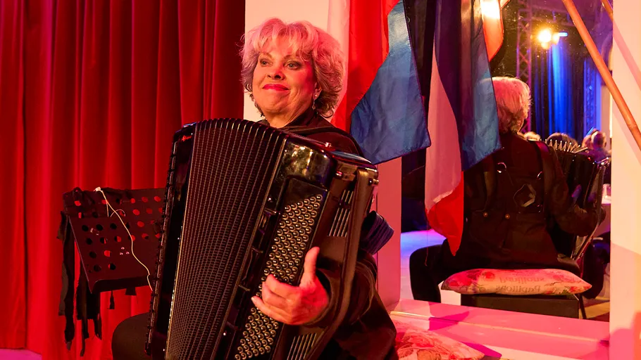 Woman playing accordion on stage with red curtains.