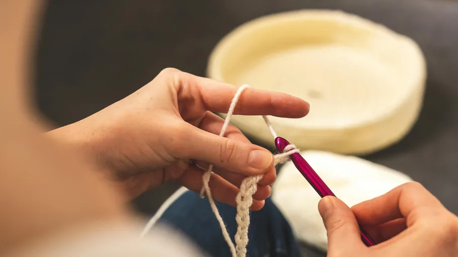 Hands crocheting with a red hook indoors.