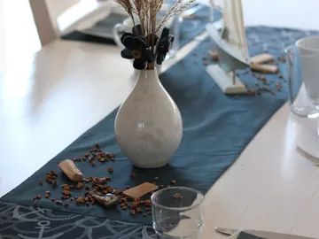 Vase mit Trockenblumen auf einem Tisch, dekoriert mit Materialien.