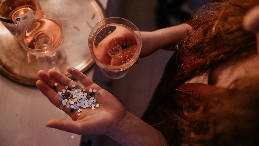 Hand holding confetti, glass of rosé wine.