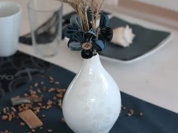 White vase decorated with dried flowers on a table.