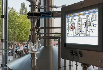 Brewery equipment with control screen and outdoor view.